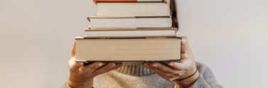 person-in-gray-sweater-carrying-a-stack-of-hardbound-books