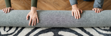 Two people rolling up a carpet on the floor