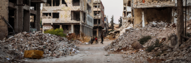 A person walking down a dirt road between two demolished buildings