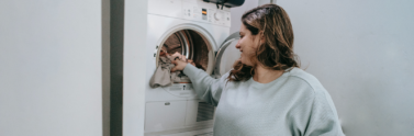 person putting clothes into top load washing machine