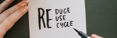 Person writing reduce, reuse, and recycle on white piece of paper