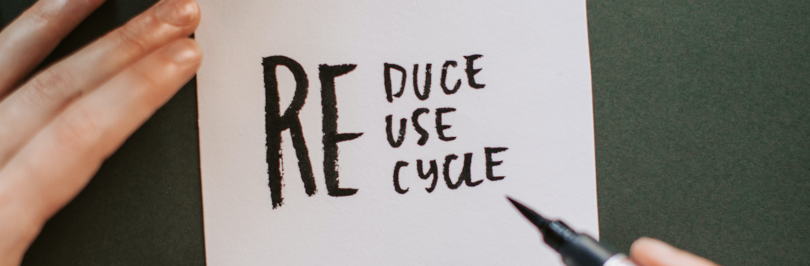 Person writing reduce, reuse, and recycle on white piece of paper