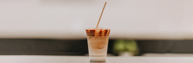 Coffee in disposable cup with straw on wooden table